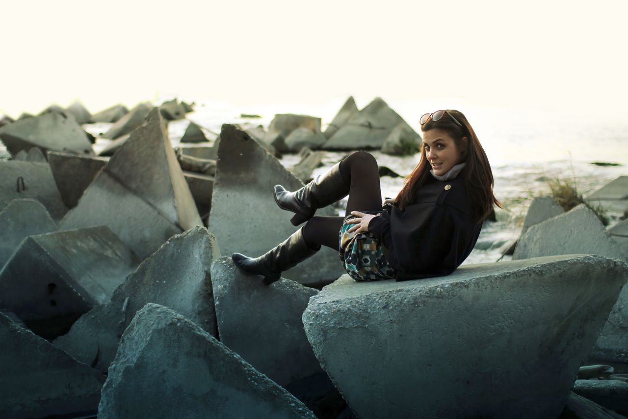 a fashionable woman in black boots posing on geometric concrete blocks