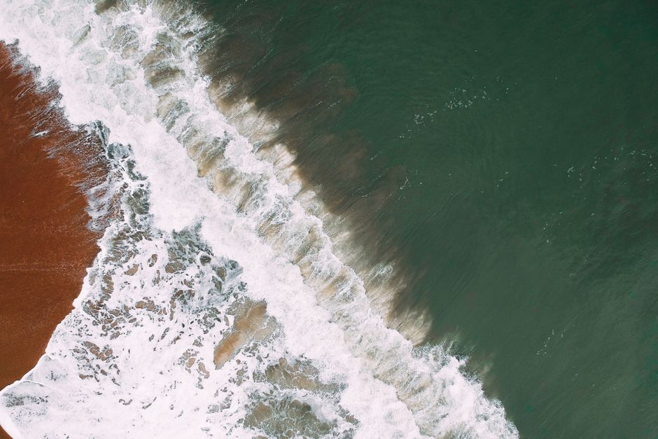 Dramatic aerial view of waves crashing onto a sandy beach shoreline.