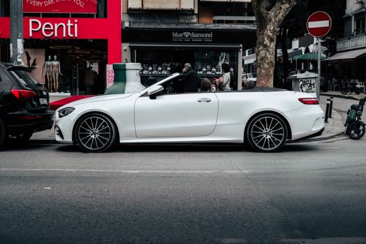 A white convertible car parked in front of shops on a city street, showcasing urban lifestyle.