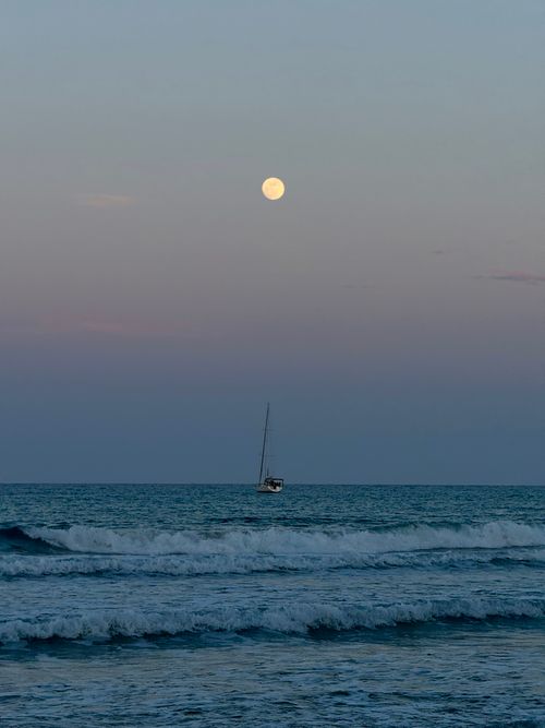 Free A tranquil evening scene of a sailboat on the ocean under a full moon. Stock Photo