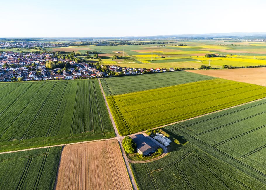 A scenic aerial capture of fields and a nearby village under a clear sky.