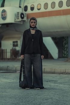 Stylish woman stands confidently near a retro airplane, urban setting.