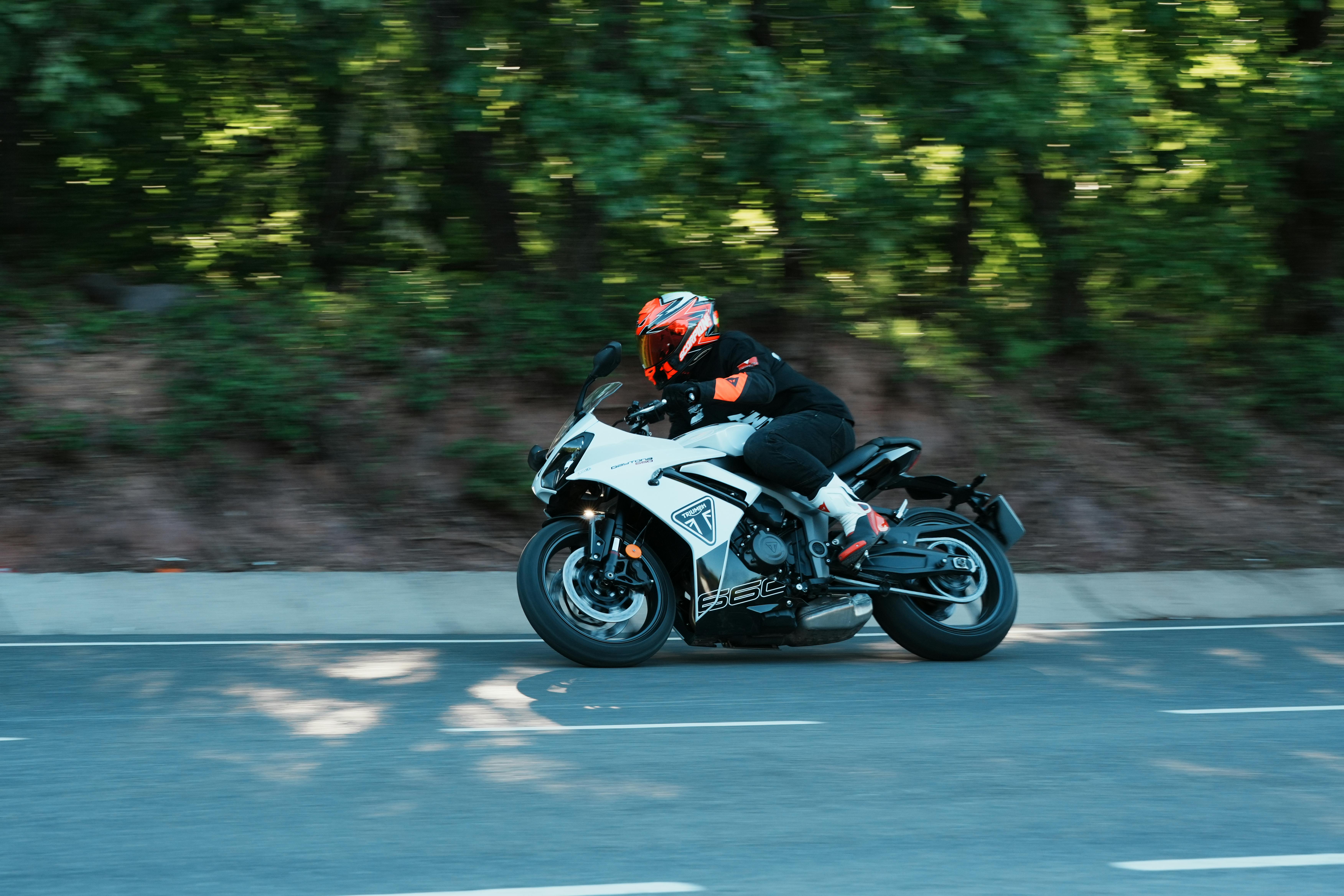 A motorcyclist in full gear riding a sport bike along a scenic road lined with trees.