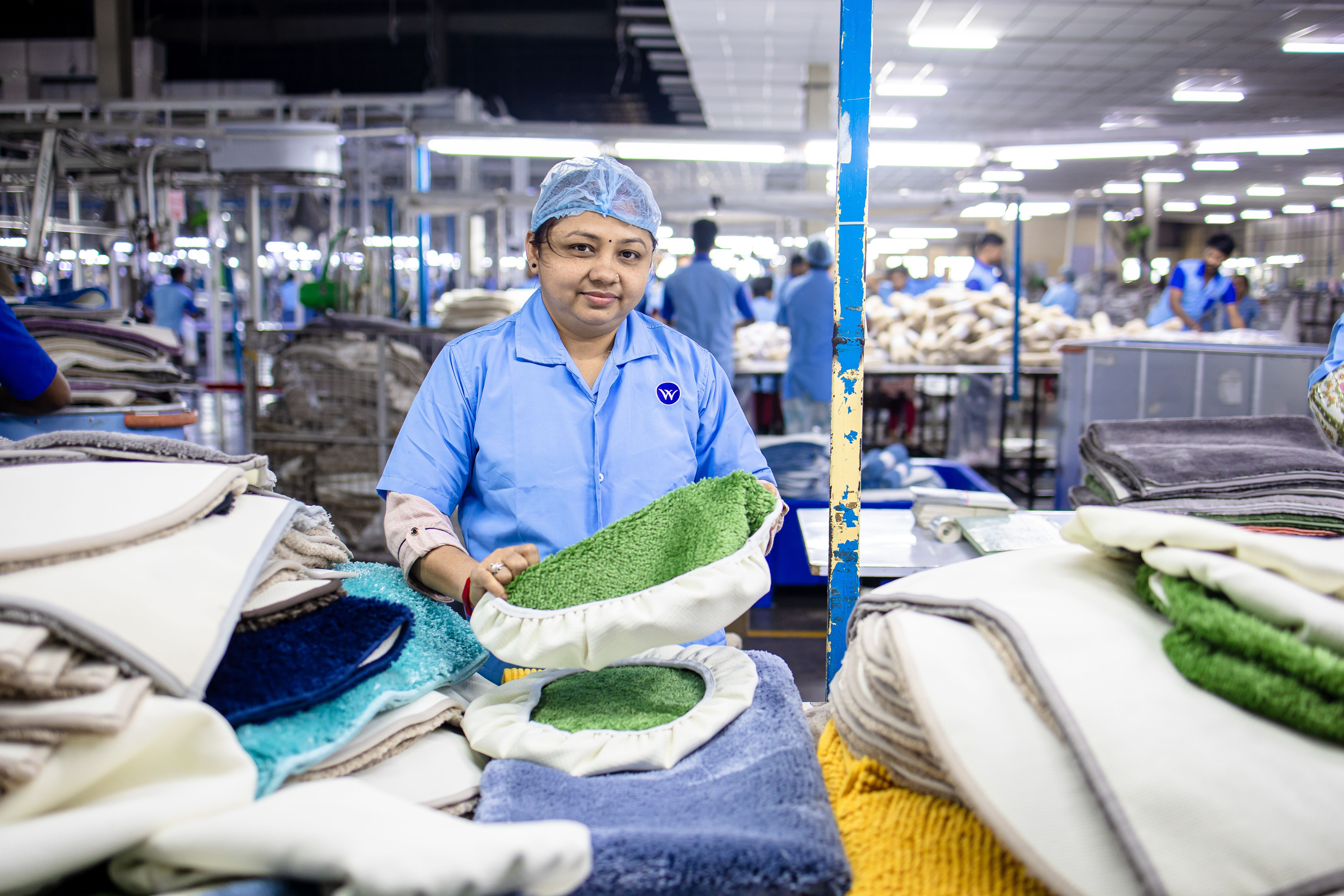 Female worker in a textile factory sorting colorful fabric pieces on a busy production floor.