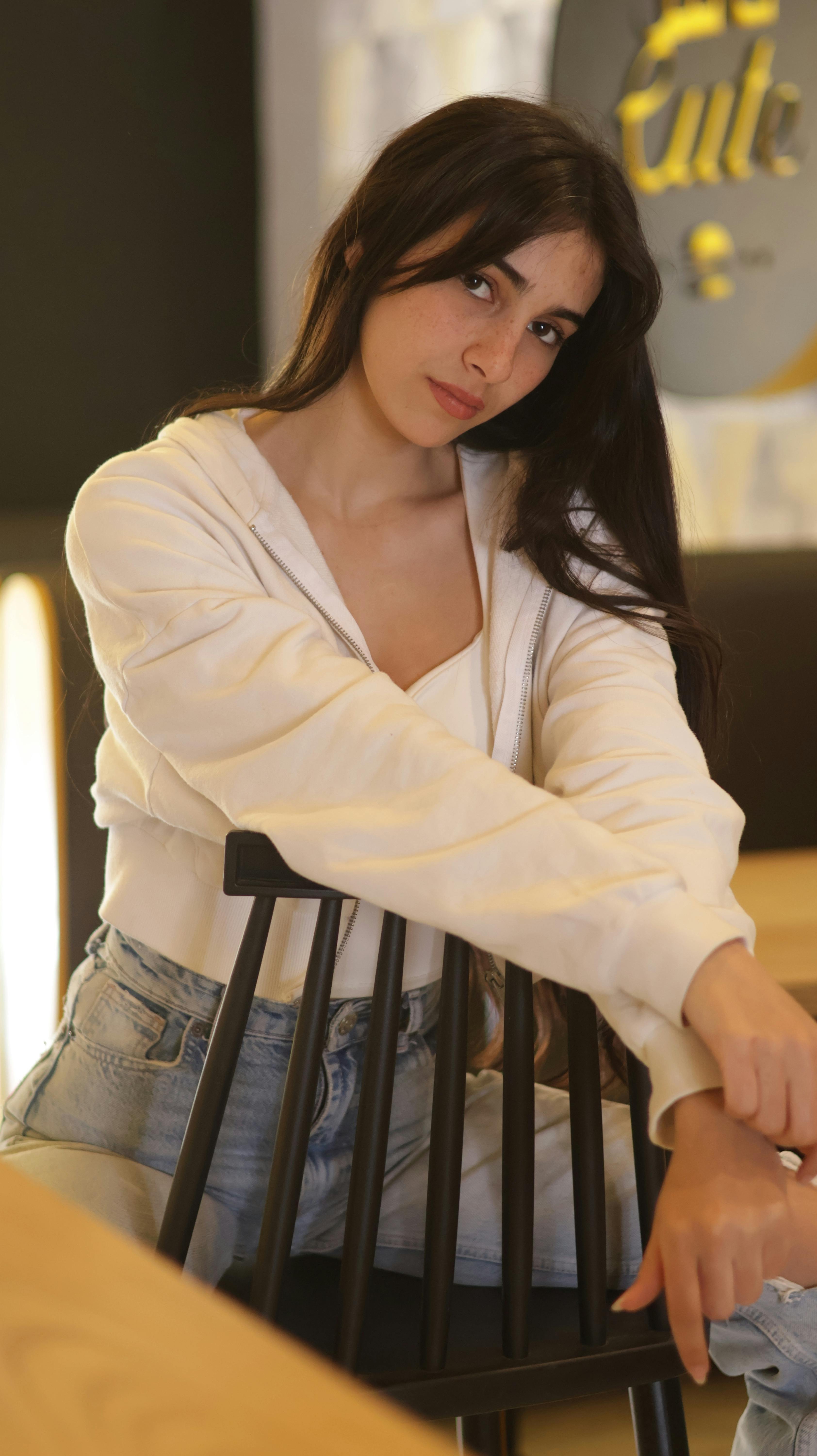 Portrait of a young woman in jeans and sweater sitting indoors. Cozy and relaxed atmosphere.