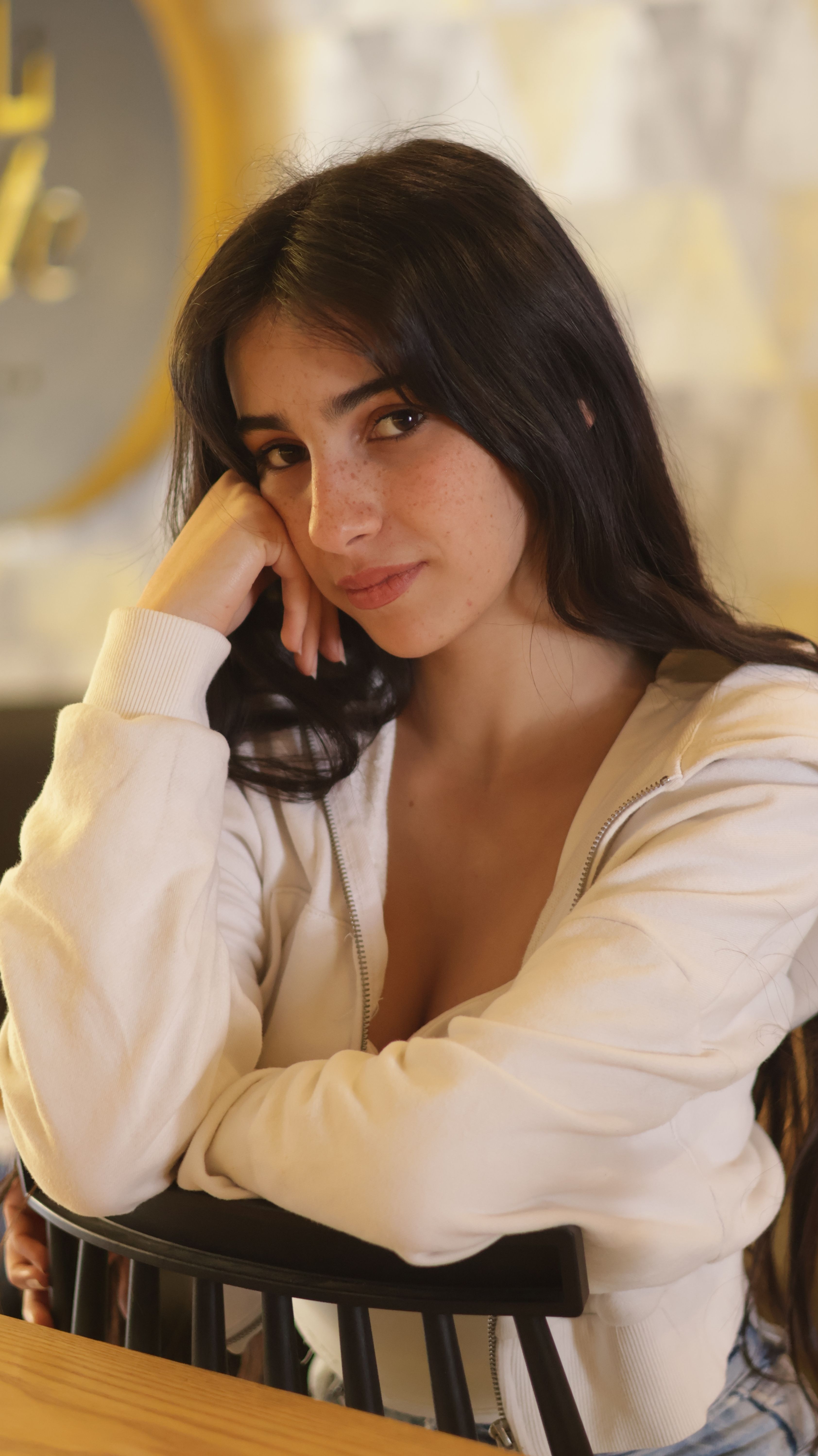 Charming portrait of a young woman sitting indoors, exuding a relaxed and thoughtful vibe.