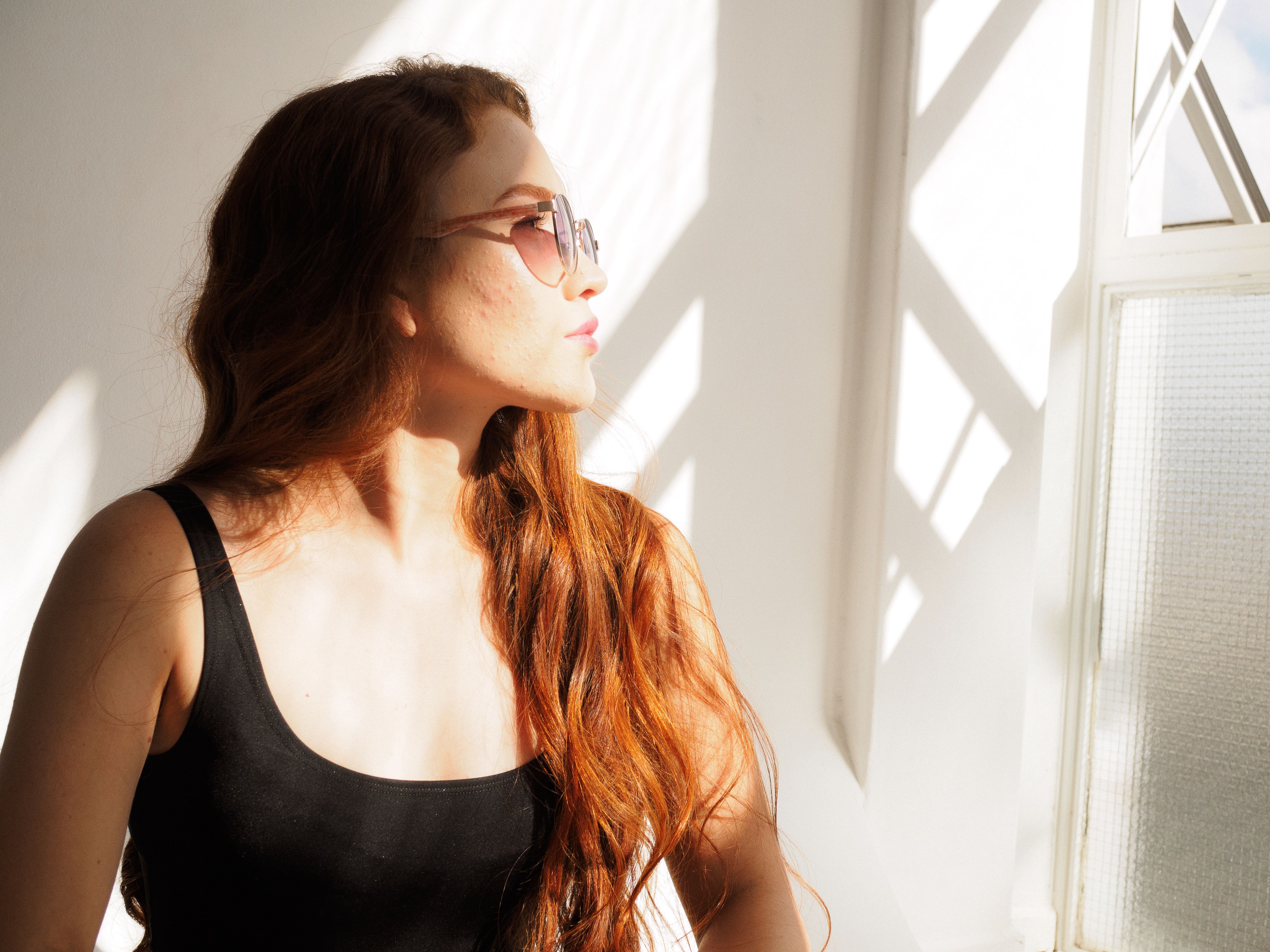Jovem mulher com óculos de sol aproveitando o sol em ambiente fechado, exalando elegância e tranquilidade.