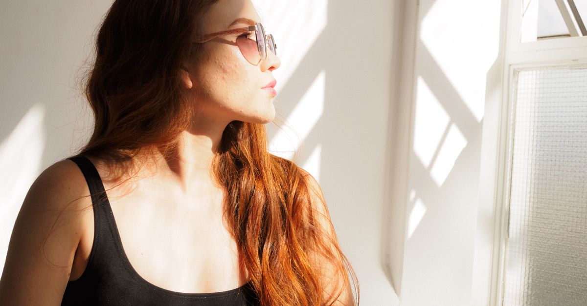 Jovem mulher com óculos de sol aproveitando o sol em ambiente fechado, exalando elegância e tranquilidade.