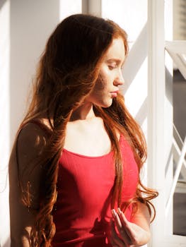 Profile of a young woman with red hair, bathed in sunlight beside a window.