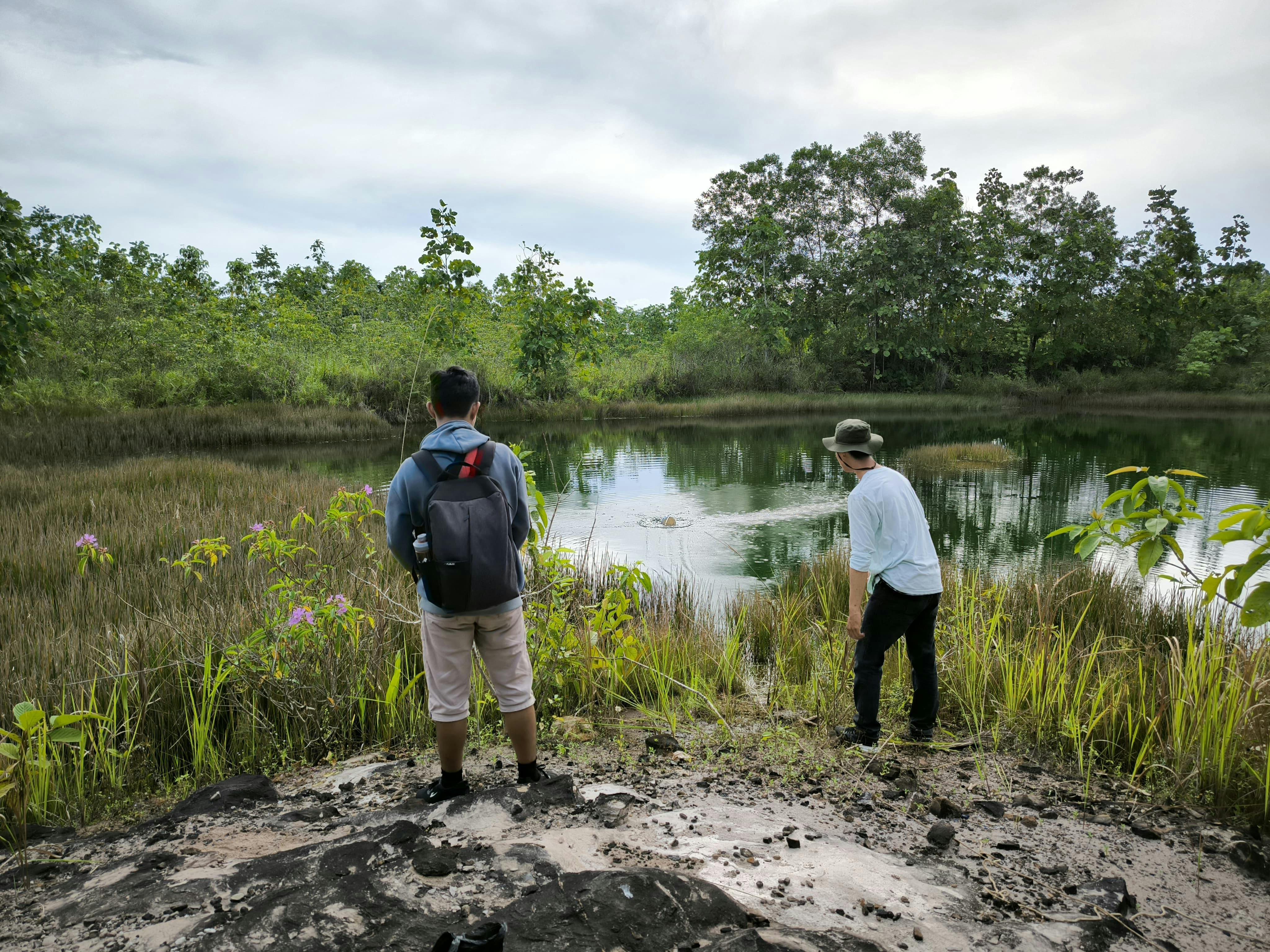 Two men stand by a calm lake surrounded by lush jungle in East Kalimantan, Indonesia.