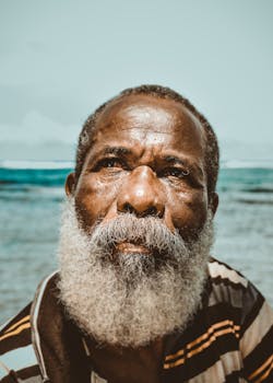 一位胡子灰白、若有所思的非洲高级男子肖像，矗立在海滩旁