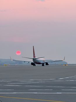 An airplane taxis on a South Korean runway at sunset, with a vivid pink sky.
