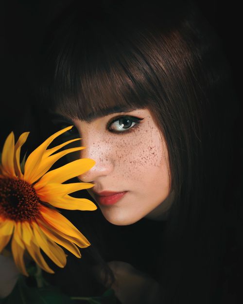 Free Striking portrait of a woman with freckles and a vivid sunflower. Stock Photo