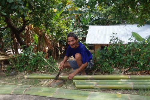 Free A cheerful man cuts bamboo outdoors in a lush, green environment. Stock Photo