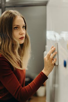 一位年轻女子身穿红色上衣，在室内中性背景下摆出深思熟虑的表情