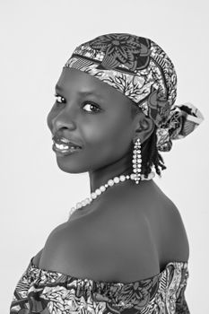 Black and white portrait of a woman wearing African print clothing, earrings, and a pearl necklace.