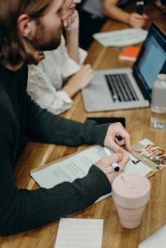 A group of people collaborating at a desk with laptops, holding a discussion in an office setting.