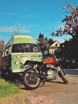 Green camper van and motorcycle parked under cherry blossoms, capturing a vintage vibe.