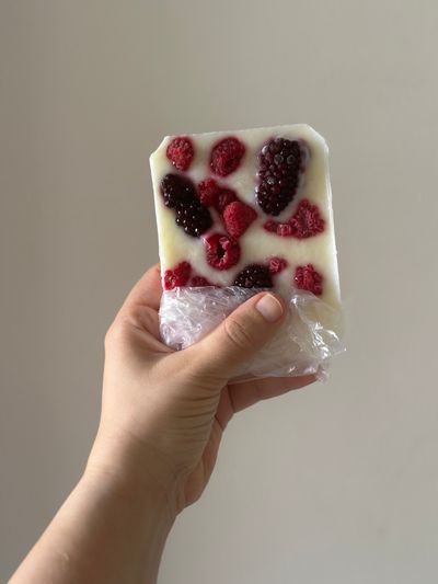A hand holding a frozen yogurt bar topped with raspberries and blackberries