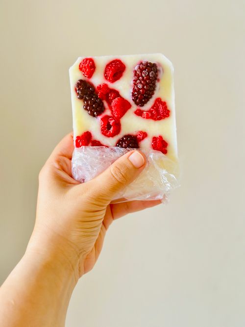 Free A hand holding a yogurt bar topped with fresh blackberries and raspberries. Stock Photo