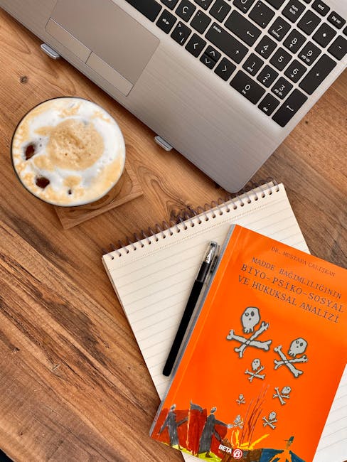 Coffee and workspace featuring a laptop, notebook, and book on a wooden desk.