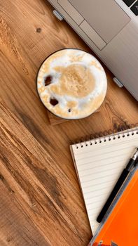 Top view of a cozy workspace with a coffee, notebook, and laptop on a wooden desk.