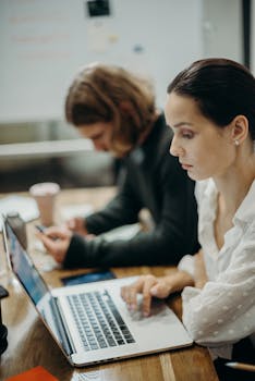 Two professionals working together at a laptop in a modern office setting.