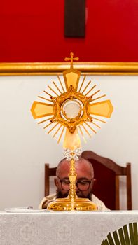 A golden monstrance displayed inside a church during a religious ceremony with a clergyman present.