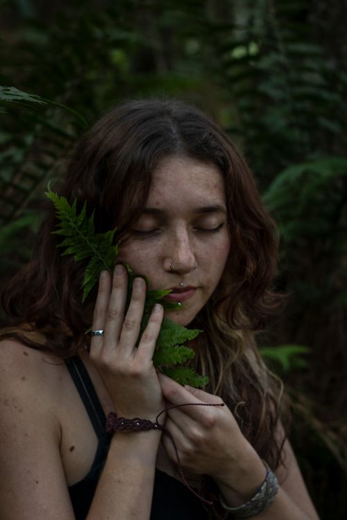 Free A woman closes her eyes while holding a fern leaf, surrounded by lush forest greenery. Stock Photo