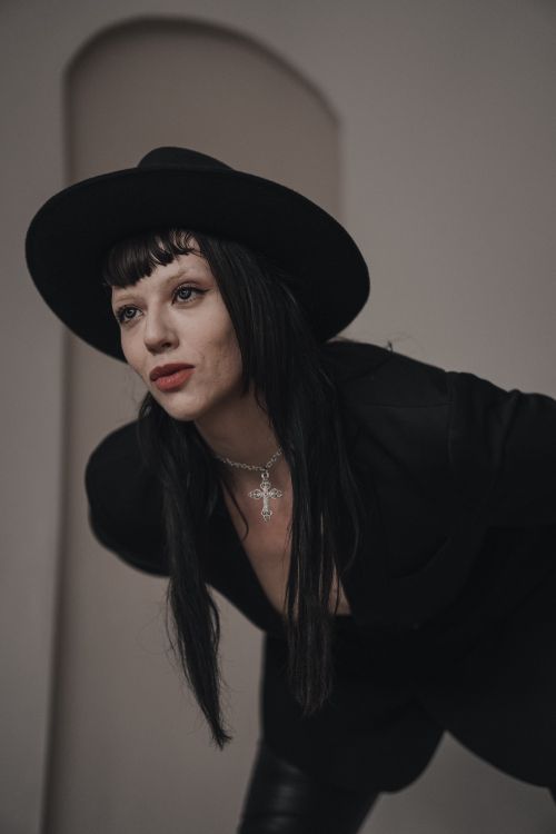 Free A fashionable woman in black attire and hat leaning forward, showcasing modern style. Stock Photo