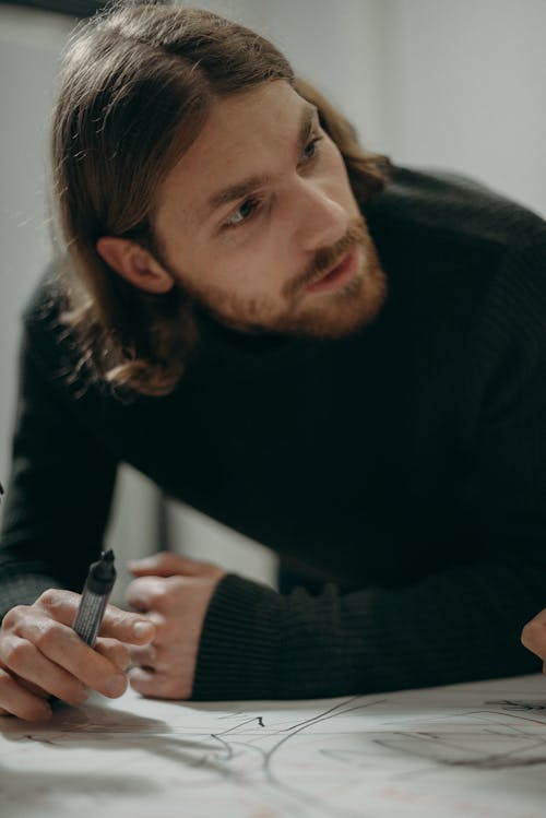 Free Man with beard and long hair concentrating while writing with a marker in an office setting. Stock Photo