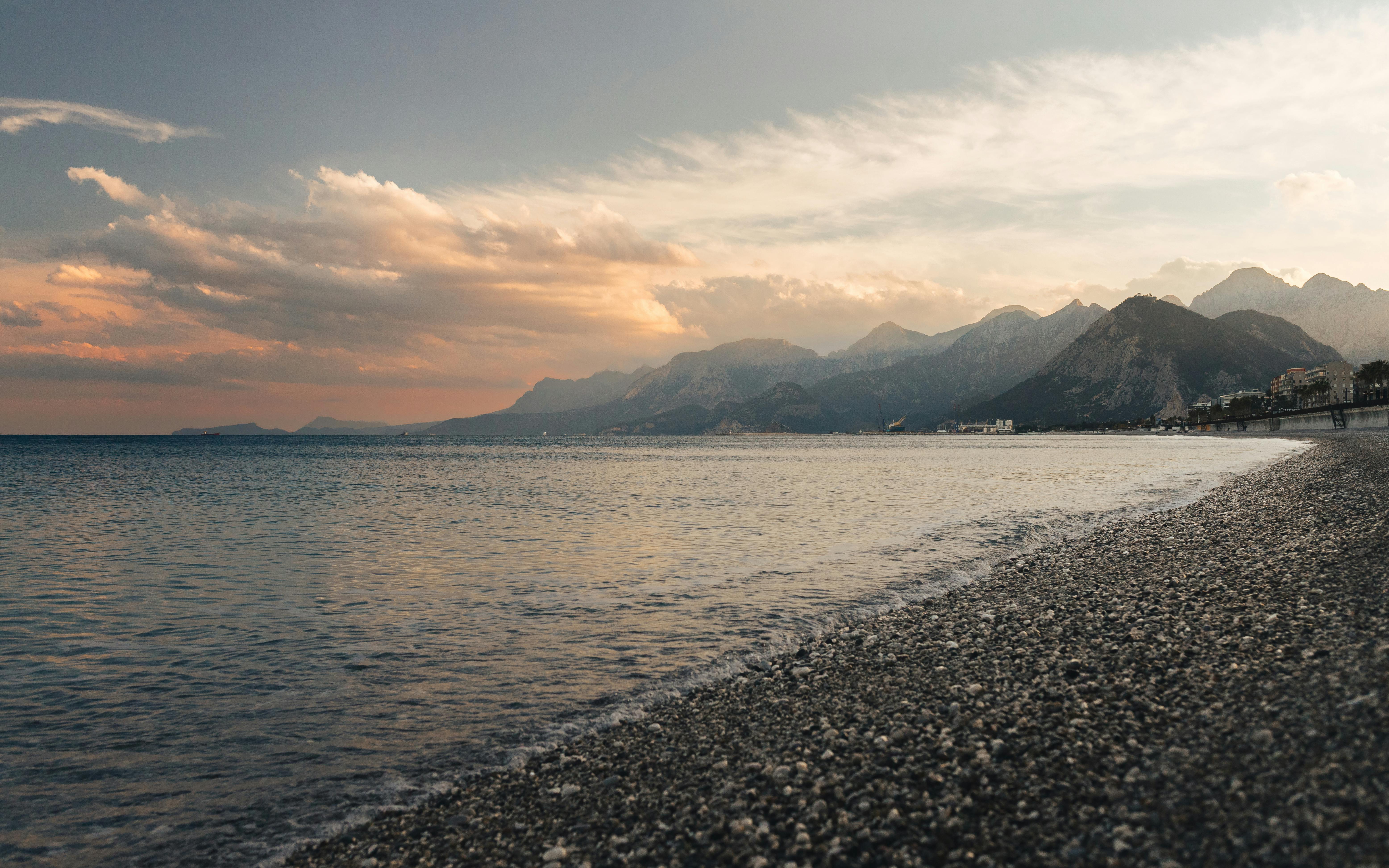 Capture of Antalya's coastline at sunset, showcasing tranquil waters and distant mountains.