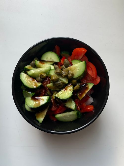 Free Top-down view of fresh cucumber and tomato salad with capers in a black bowl. Stock Photo