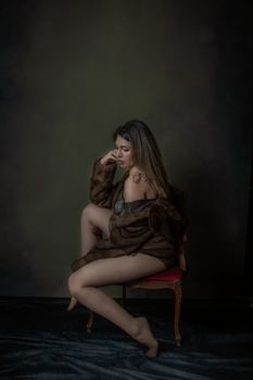 Elegant woman in fur coat sitting on chair, dimly lit portrait.