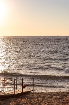 Tranquil sunset over ocean with a wooden pier in view, casting a warm glow.