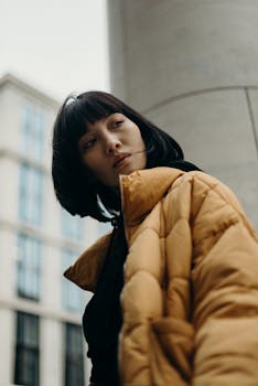 Stylish urban portrait of a woman wearing a yellow puffer jacket, gazing thoughtfully.