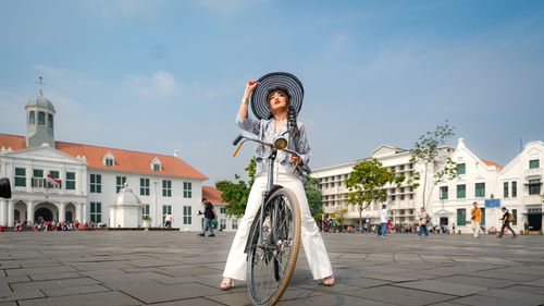 Free A fashionable woman poses with a vintage bicycle in Jakarta's Kota Tua, surrounded by historic colonial architecture. Stock Photo