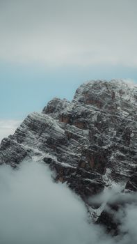A stunning snow-capped mountain peak emerging through misty clouds under a serene blue sky.