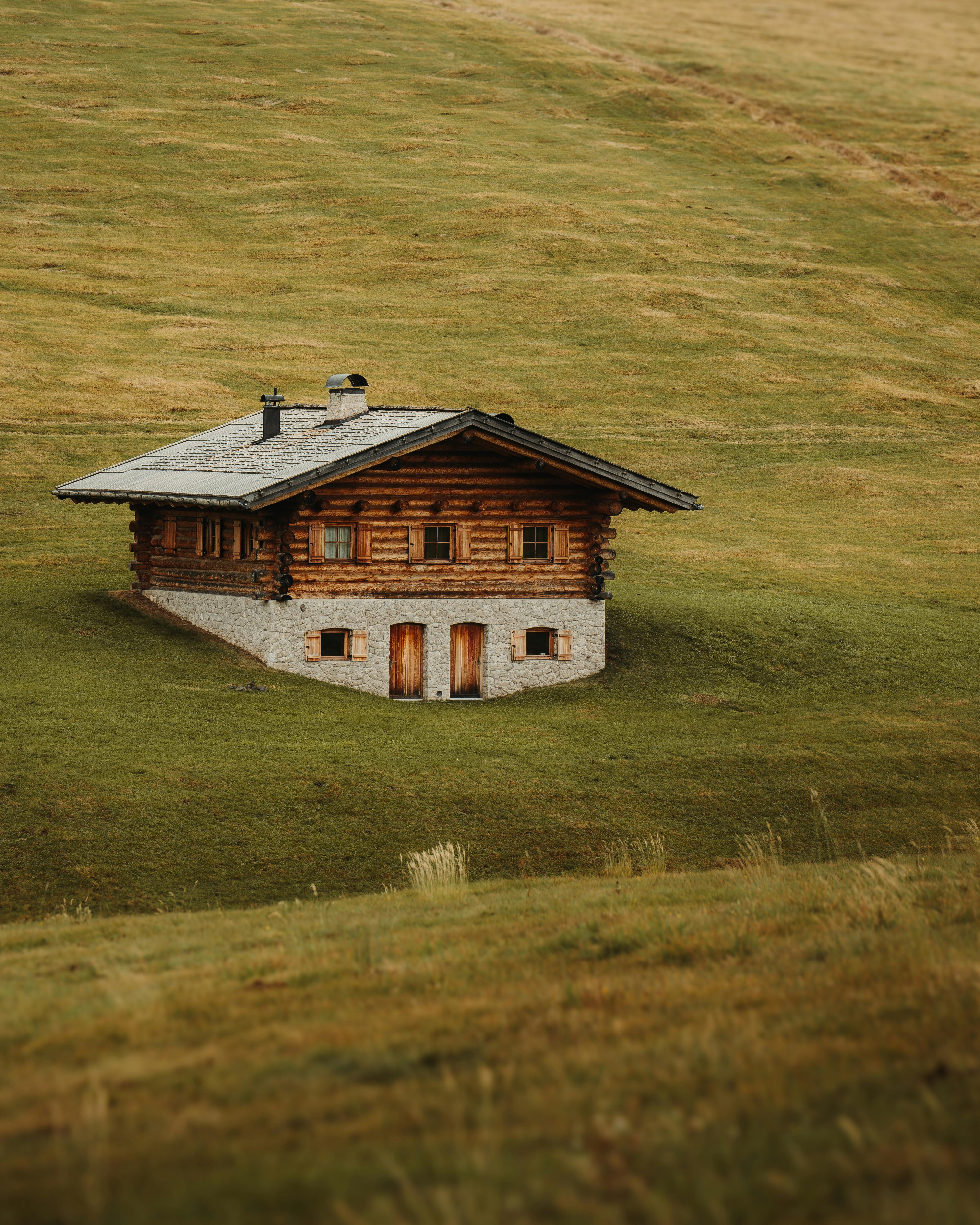 A serene rustic cabin nestled in vibrant green hills on a calm day, showcasing nature's tranquility.