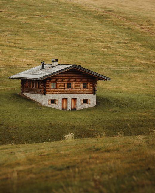 A serene rustic cabin nestled in vibrant green hills on a calm day, showcasing nature's tranquility.