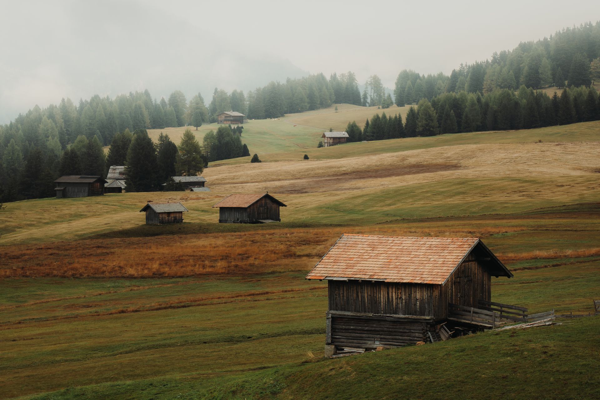 Idyllic rural scene with wooden cabins in misty mountainous landscape showcasing serene natural beauty.