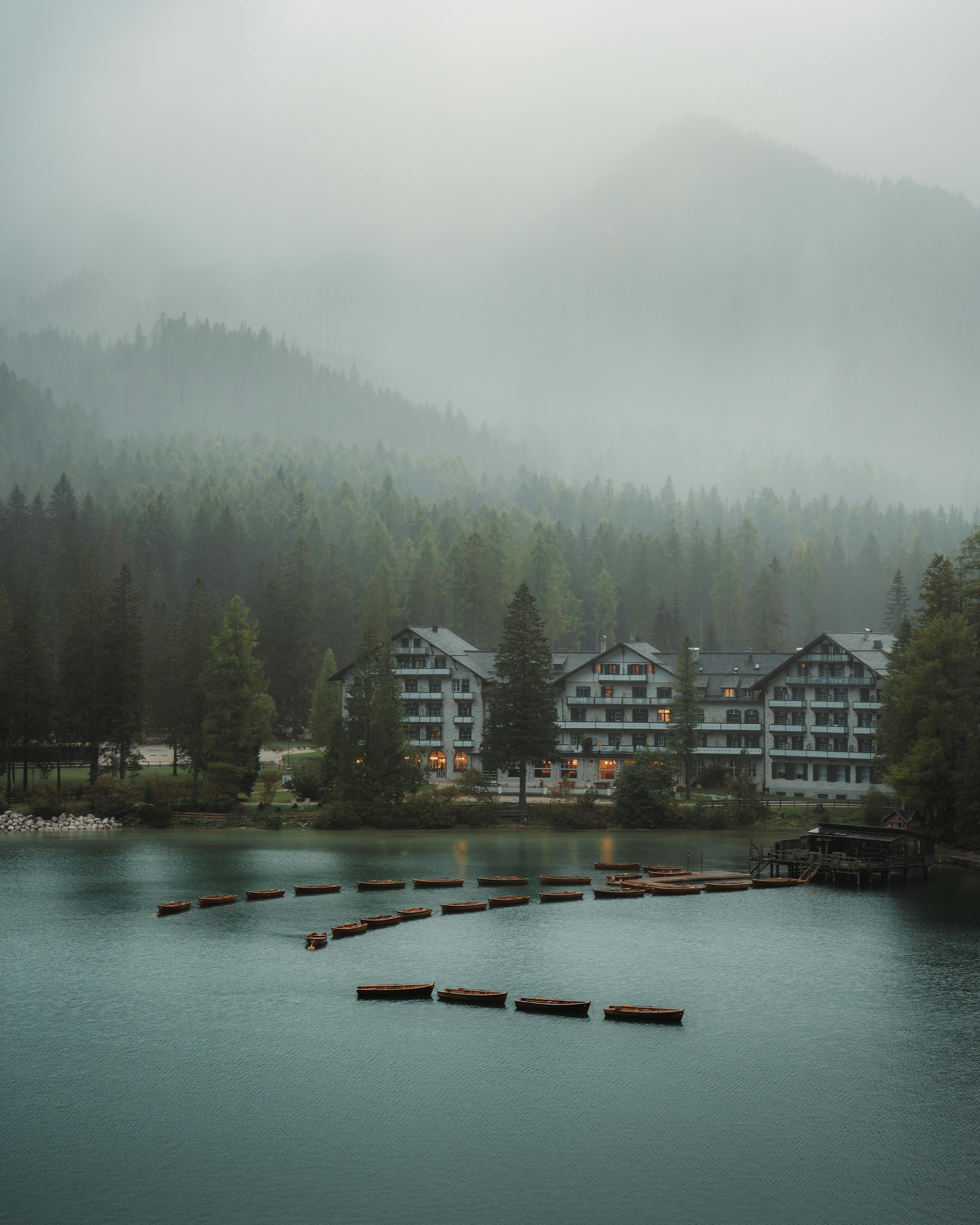 A serene misty morning at a lakeside hotel surrounded by forested mountains.