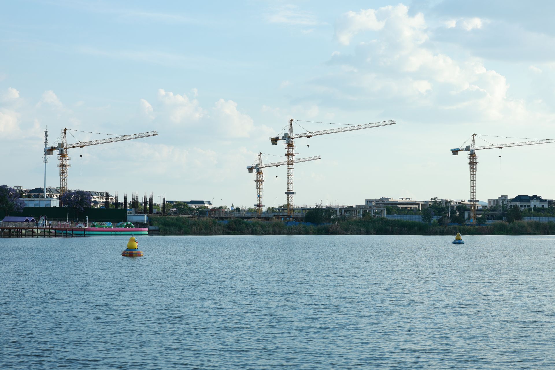 Construction cranes by a riverside under a clear sky, showcasing urban development.
