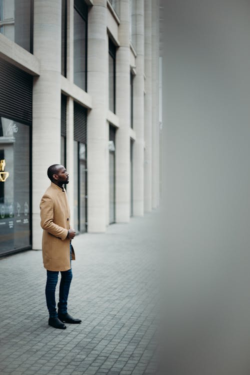 Side View Photo of Man in Brown Coat Posing Outside Building