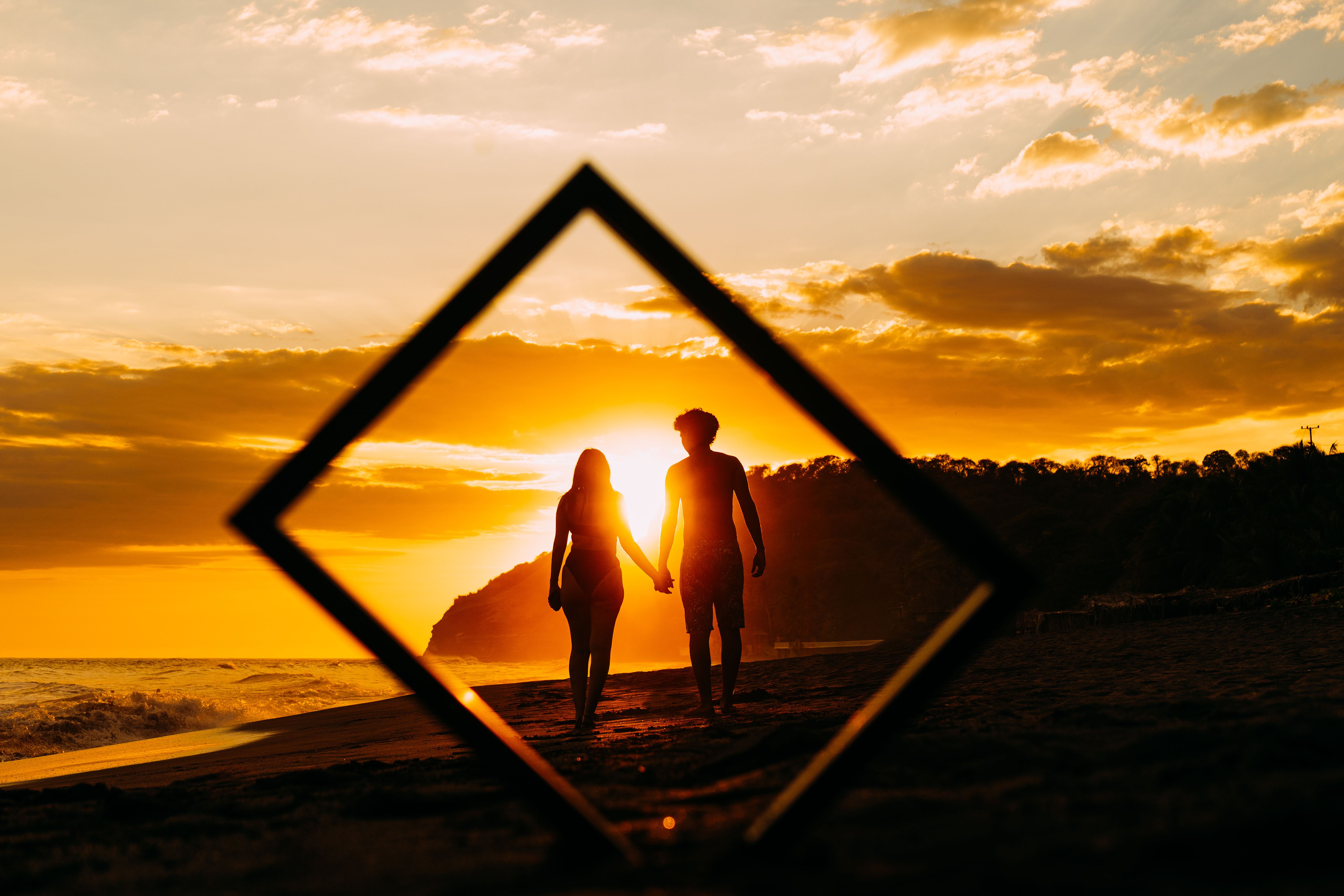 Silhouette of a couple holding hands on a beach during a vibrant El Salvador sunset.