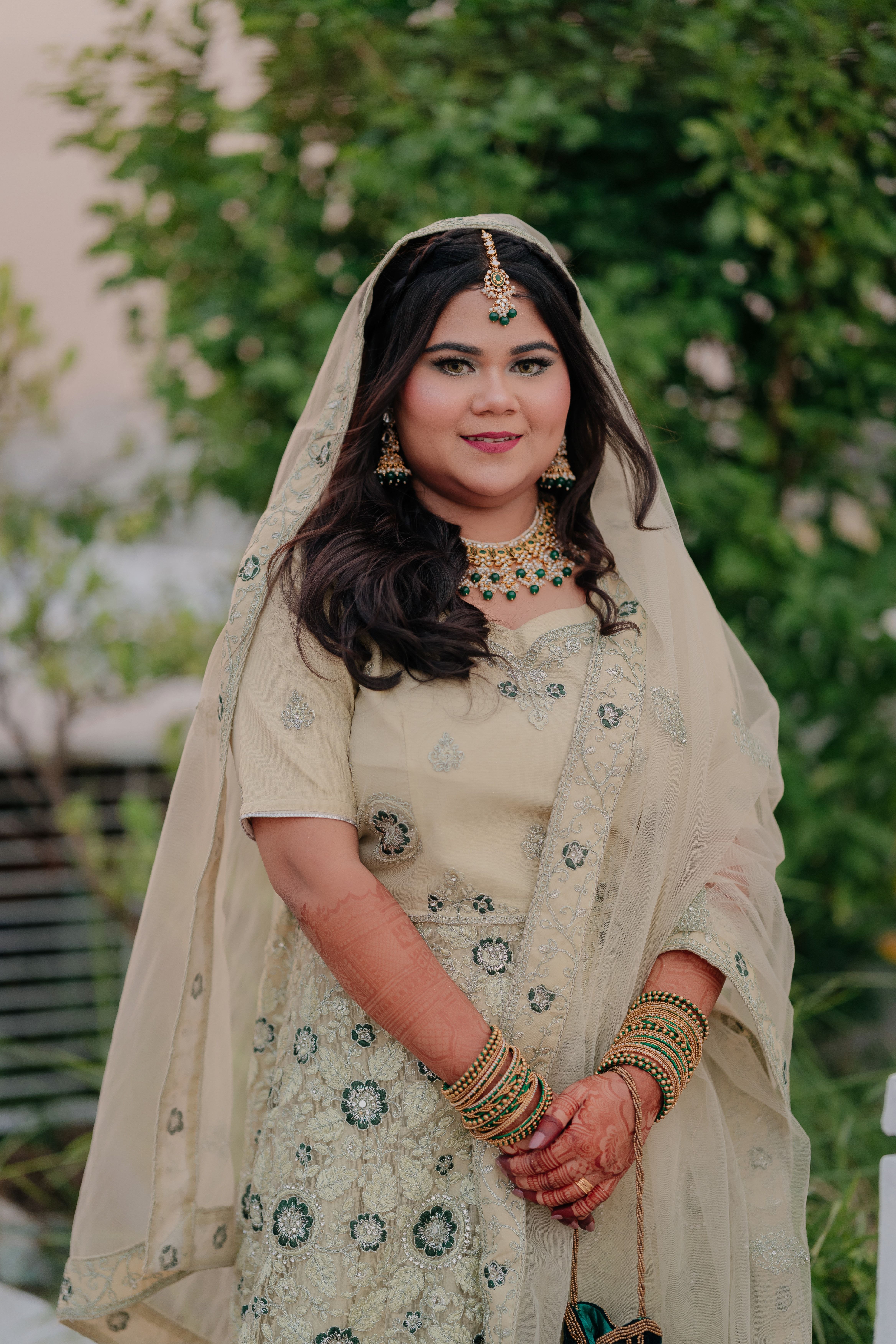 Beautiful bride in traditional South Asian wedding outfit with ornate jewelry, captured outdoors.
