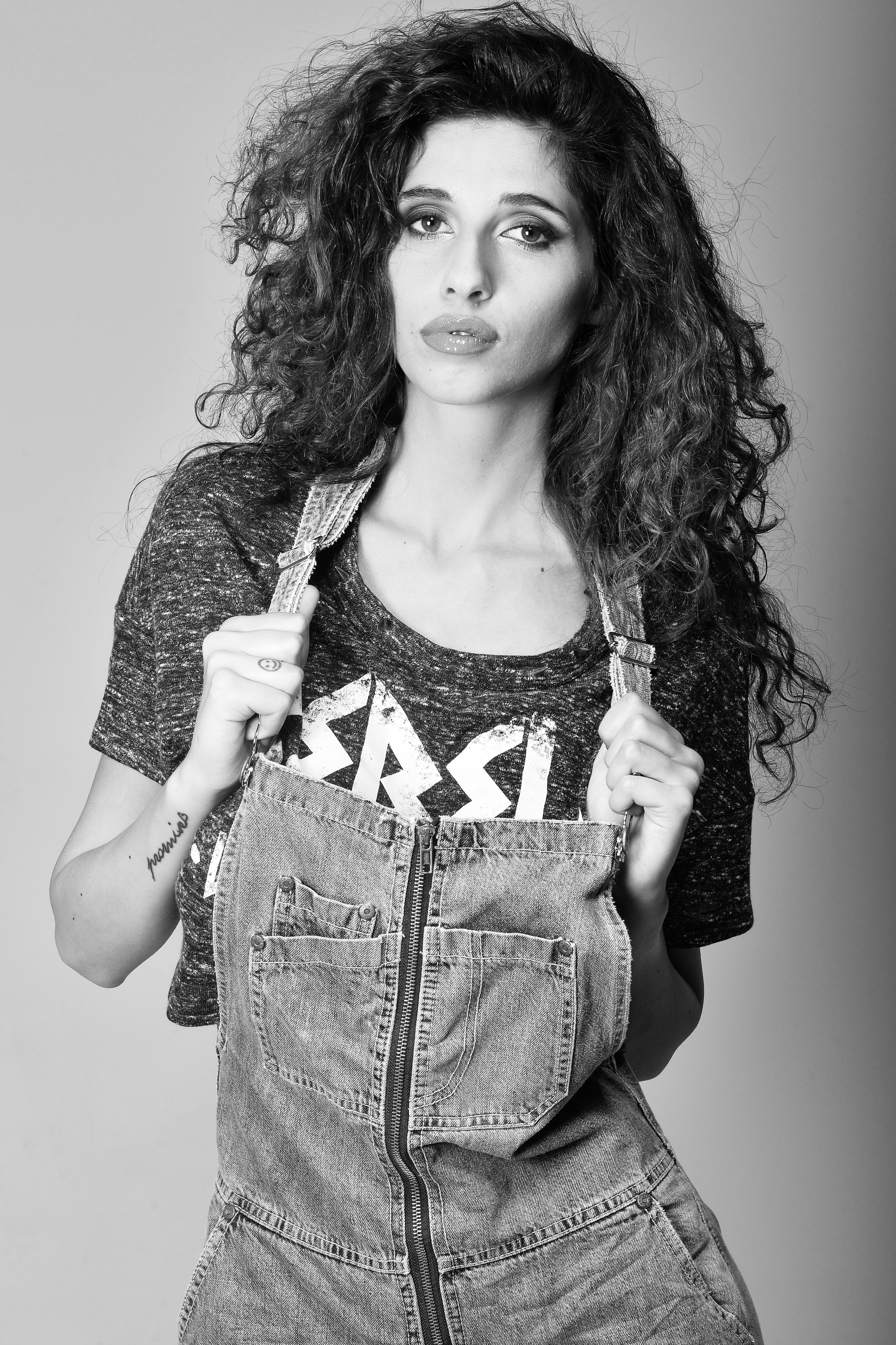 Black and white portrait of a woman in denim overalls and a printed t-shirt.