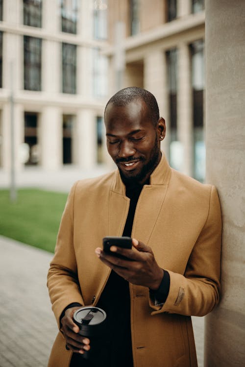 Free Selective Focus Photo of Smiling Man Looking at His Phone While Holding Cup  Stock Photo