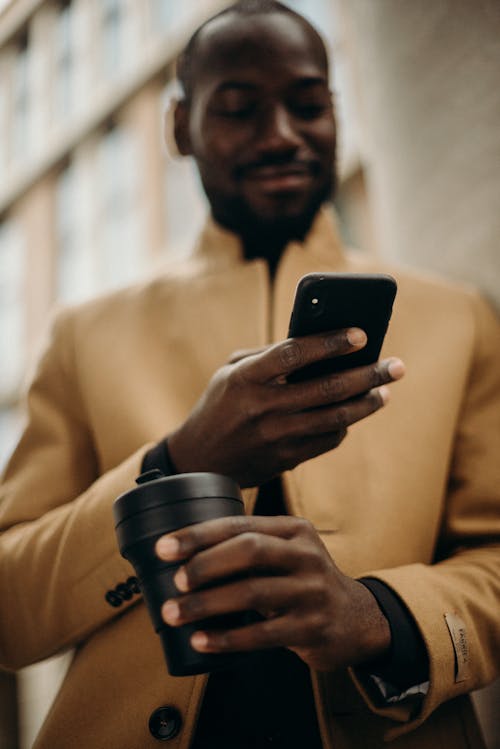 Selective Focus Photo of Smiling Man Looking at His Phone While Holding Cup