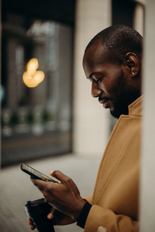 Free Side view of a man holding a coffee cup and smartphone, dressed in a coat. Stock Photo